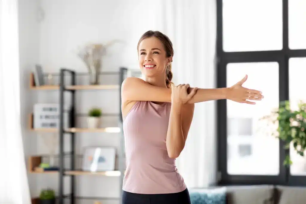 women stretching to stay active and healthy, sport, fitness and healthy lifestyle concept - smiling young woman stretching arm at home